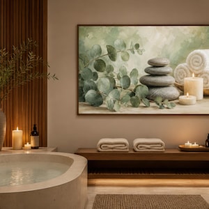 May include: A rectangular wall art print featuring a stack of smooth grey stones, green eucalyptus branches, and rolled white towels. The artwork is displayed in a spa-themed room with a bathtub, wooden bench, and lit candles, creating a calm atmosphere.