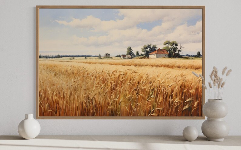 a serene rural landscape with a vast golden wheat field stretching out under a blue sky dotted with fluffy white clouds. In the distance, a small white house can be seen nestled among the trees. The scene is framed by a white border, and a white vase and a small white sculpture are placed on a white surface to the right of the frame.