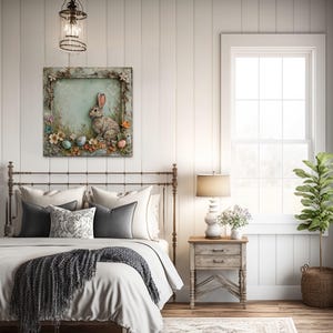 a cozy bedroom with a large bed, a wooden nightstand, and a painting of a rabbit on the wall. The room has white walls, a wooden floor, and a window with white curtains. There is also a potted plant and a lamp in the room.