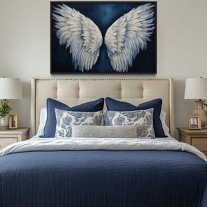 a bedroom with a large bed, a framed artwork of white wings on the wall above it, and two nightstands with lamps on either side.