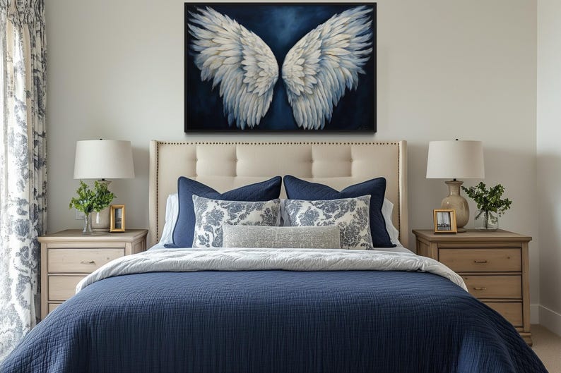 a bedroom with a large bed, a framed artwork of white wings on the wall above it, and two nightstands with lamps on either side.