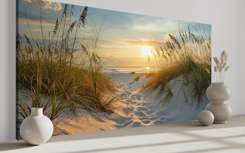 a serene beach scene with tall grasses swaying in the foreground and a path leading to the beach in the distance, with the sun setting over the horizon.