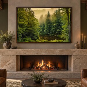 May include: A rectangular framed wall art print depicting a dense green forest with a calm river and misty atmosphere, mounted above a stone fireplace with a burning fire, flanked by two brown leather armchairs and a round wooden table.