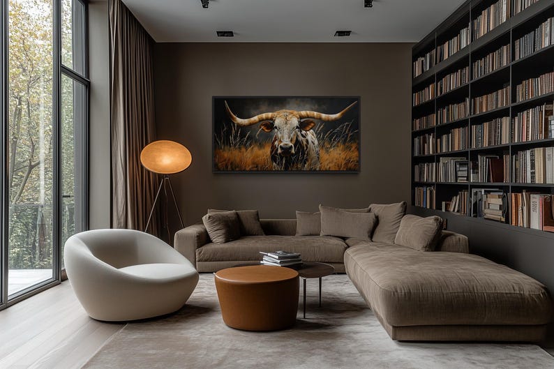 a modern living room with a large window overlooking trees, a comfortable sofa, a round coffee table, and a large painting of a bull's head on the wall.