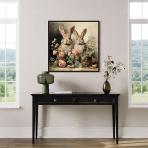 a living room with a black console table in the center, which has a vase, a lamp, and a book on it. Above the table, there is a framed painting of two rabbits sitting next to each other, surrounded by flowers. The room has large windows that provide a view of a green field and trees outside.