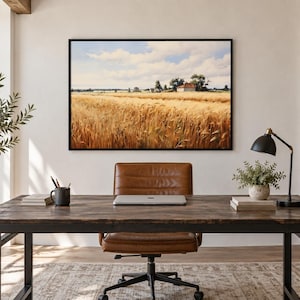 May include: A rectangular wall art print in a black frame depicting a golden wheat field under a blue sky with clouds, mounted on a white wall above a dark wood desk with a brown leather office chair, a laptop, and a black desk lamp.