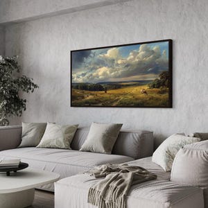 a living room with a large landscape painting hanging on the wall above a gray sofa. The painting features a countryside scene with a cloudy sky and rolling hills. The room has a minimalist and modern design, with a white coffee table and a potted plant adding a touch of greenery to the space.