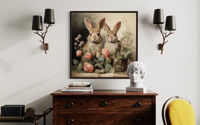a wooden dresser with a framed painting of two rabbits sitting in a basket of flowers hanging on the wall above it. The dresser also has a statue of a man's head and some books on top.