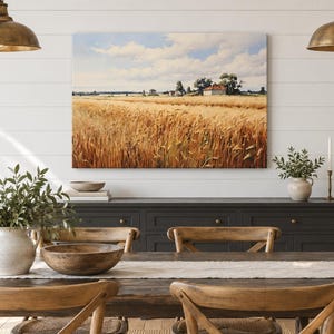 May include: A rectangular canvas wall art print depicting a golden wheat field under a blue sky with white clouds, featuring a small house in the distance. The artwork is displayed on a white shiplap wall above a dark gray wooden sideboard.