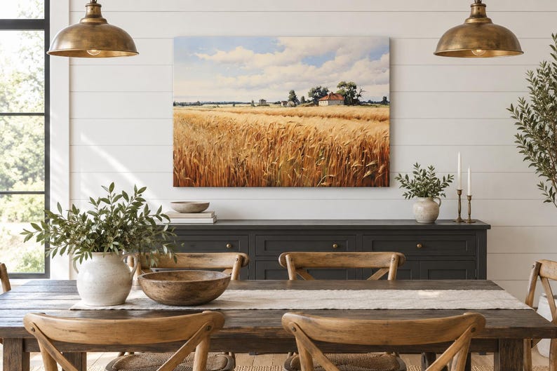 May include: A rectangular canvas wall art print depicting a golden wheat field under a blue sky with white clouds, featuring a small house in the distance. The artwork is displayed on a white shiplap wall above a dark gray wooden sideboard.