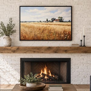 May include: A rectangular landscape wall art print featuring a golden wheat field under a blue sky with white clouds, displayed in a thin black frame above a rustic wooden fireplace mantel and a white brick fireplace with a burning fire inside.
