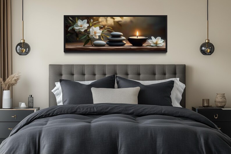 a serene bedroom scene with a gray tufted headboard, a gray comforter, and a gray throw pillow. Above the bed, there is a framed artwork featuring a still life of stones, flowers, and a lit candle. The room has a neutral color palette with a touch of greenery from the potted plant and vases.