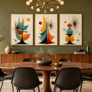 May include: A set of three framed wall art prints featuring abstract geometric shapes in teal, orange, and black on a cream background. The artwork displays starburst patterns, curved lines, and circular motifs, displayed in a dining room.