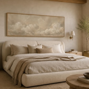 Pode incluir: Um quarto com uma cama grande com roupa de cama e almofadas creme. Uma pintura de paisagem de nuvens está pendurada acima da cama. Mesas de cabeceira de madeira com lâmpadas em ambos os lados. Uma mesa de centro redonda de madeira e uma janela grande também são visíveis.