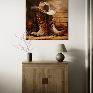 a wooden cabinet with a lamp on top, and a painting of a cowboy hat and boots hanging on the wall above it.