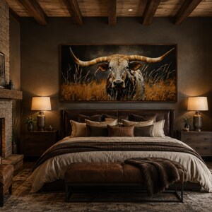 May include: A luxurious bedroom with a rustic theme. A large painting of a longhorn bull hangs above a bed with brown leather headboard and multiple pillows. A fireplace and leather chair are visible on the left, with lamps on either side of the bed.