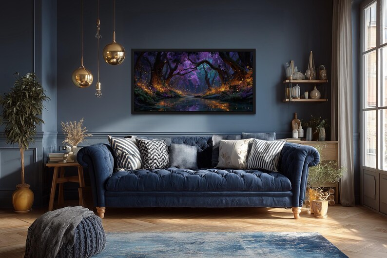 Op de afbeelding: Een donkerblauwe bank met kussens staat tegen een donkerblauwe muur. Boven de bank hangt een ingelijst landschapsschilderij met een bossc&egrave;ne in paarse en oranje tinten. Gouden hanglampen hangen aan het plafond.