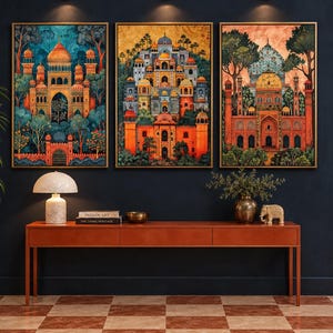 May include: Three framed rectangular wall art prints featuring intricate architectural structures with domes and arches in vibrant orange, blue, and gold tones, displayed above a long, narrow, orange wooden console table with books and decor.