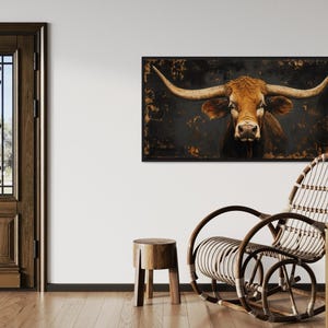 a rustic interior with a wooden door, a large framed picture of a bull's head hanging on the wall, a wicker chair, and a wooden stool.