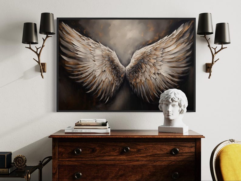 a large framed painting of a pair of angel wings hanging on a wall above a wooden dresser. The dresser has a bust of a person and some books on top of it. There are also two black lamps on either side of the painting.
