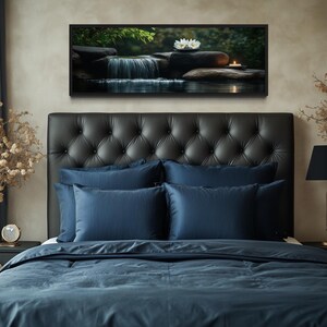a serene bedroom scene with a large bed adorned with blue bedding and a tufted headboard. Above the bed, a framed picture of a waterfall and flowers adds a touch of nature to the room. The bed is positioned next to a nightstand with a lamp and a vase of flowers, creating a cozy and inviting atmosphere.
