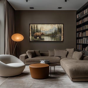 a cozy living room with a large window overlooking a scenic outdoor view. The room is furnished with a comfortable sofa, a round coffee table, and a floor lamp. A large bookshelf filled with books is also present, creating a warm and inviting atmosphere. A framed painting of a bear in a forest setting adds a touch of nature and artistry to the space.