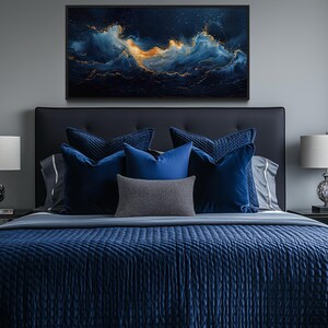a luxurious bedroom with a large bed adorned with blue and gray bedding, flanked by two nightstands with lamps. Above the bed, a large framed artwork of a night sky with swirling clouds and stars is displayed on the wall.