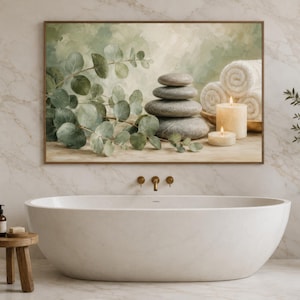 May include: A rectangular wall art print featuring a stack of four smooth grey stones, green eucalyptus branches, two white rolled towels, and two lit pillar candles. The artwork is displayed in a bathroom above a white oval freestanding bathtub.