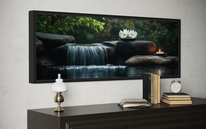 A framed photograph of a serene waterfall and lotus flowers is displayed on a wall above a wooden dresser with a lamp, books, and a clock.