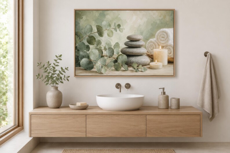 May include: A rectangular framed wall art print featuring a stack of four smooth grey stones, a sprig of green eucalyptus leaves, two lit cylindrical candles, and three rolled white towels against a soft, muted green and beige background.