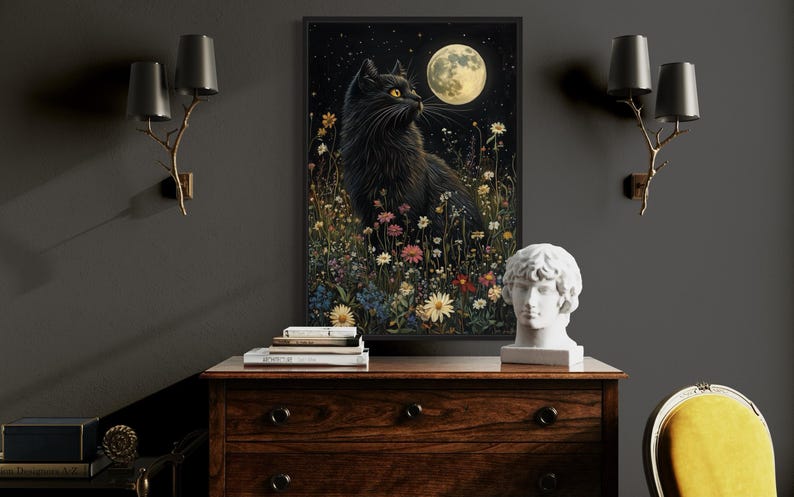 a black cat sitting in a field of flowers, with a full moon in the background. The cat is surrounded by various flowers and plants, creating a serene and peaceful scene. The image is framed and displayed on a wooden dresser, which also has a statue and some books on it. The dresser is situated in a room with a gray wall and two wall sconces.
