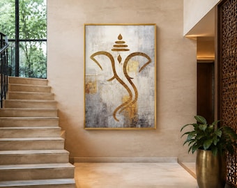 May include: A rectangular wall art piece featuring a stylized gold Ganesha outline centered on a textured background of gray, white, and metallic gold patches. The artwork is enclosed in a thin gold frame and displayed on a neutral beige wall.