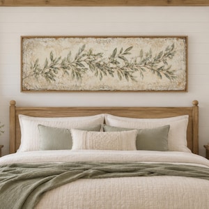May include: A bedroom scene featuring a wooden bed frame, nightstands, and a large framed artwork above the bed. The artwork depicts a botanical design in muted green and beige tones. The bed is made with neutral-colored bedding and a green throw.