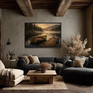 May include: A framed landscape painting depicts a wooden boat docked on a pier at a lake. The artwork hangs above a dark gray sectional sofa with beige pillows. The room has a rustic, cozy aesthetic with wooden beams and a large window.