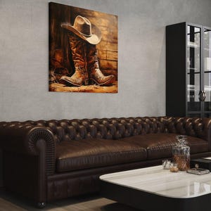 a cozy living room with a brown leather couch, a white coffee table, and a framed painting of a cowboy boot and hat on the wall.