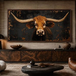 May include: A large rectangular wall art piece featuring a detailed portrait of a brown longhorn bull with expansive horns against a dark, textured black and copper background, framed in a thin dark wood border, centered above a long wooden cabinet.