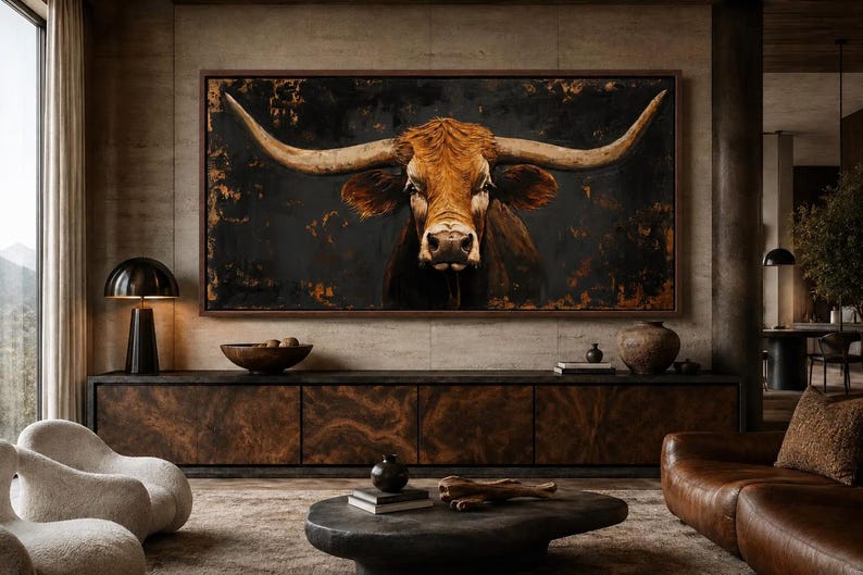 May include: A large rectangular wall art piece featuring a detailed portrait of a brown longhorn bull with expansive horns against a dark, textured black and copper background, framed in a thin dark wood border, centered above a long wooden cabinet.