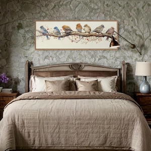 May include: A bedroom scene featuring a large wooden bed with a beige comforter and pillows. Above the bed is a framed artwork depicting several colorful birds perched on a branch. The walls are a textured, muted green.