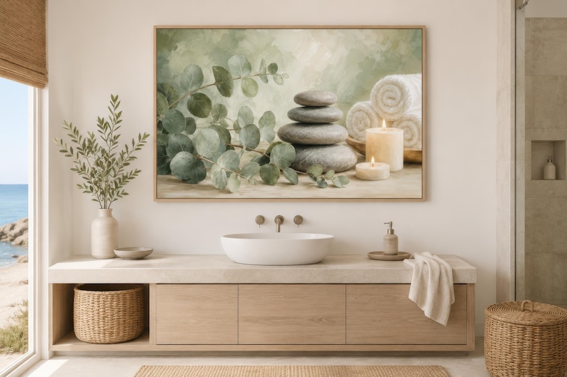 May include: A rectangular wall art print in a light wood frame featuring a painted scene of a stack of four smooth grey stones, green eucalyptus branches, two white pillar candles, and three rolled white towels against a soft green background.
