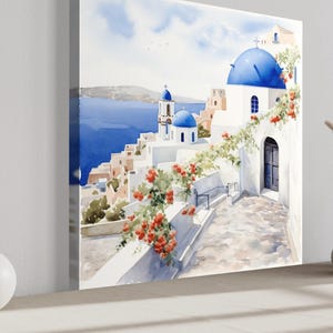 a large painting of a picturesque Greek island with white buildings, blue domes, and a blue sky with clouds. The painting is displayed on a wall, and there are two white vases and a small white sculpture placed in front of it.