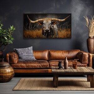 a living room with a large brown leather couch, a wooden coffee table, and a framed painting of a bull with large horns hanging on the wall above the couch.