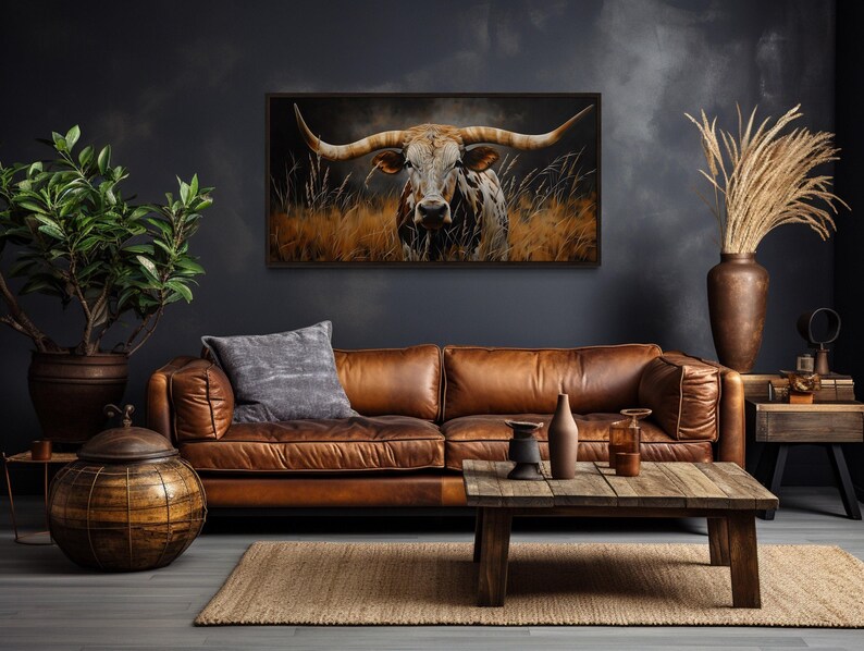a living room with a large brown leather couch, a wooden coffee table, and a framed painting of a bull with large horns hanging on the wall above the couch.
