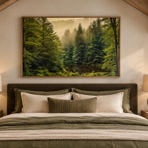 May include: A rectangular wall art print featuring a dense forest with tall green pine trees and a misty, golden-hued atmosphere. The artwork is displayed in a thin wooden frame, centered above a bed with olive green bedding and pillows.