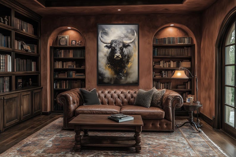 a cozy living room with a large brown leather sofa, a wooden coffee table, and a bookshelf filled with books. A large painting of a bull's head is prominently displayed on the wall above the sofa.