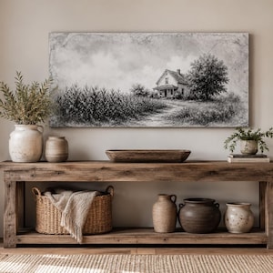 Peut inclure: Une œuvre d'art murale rectangulaire représentant une ferme dans un champ, exposée au-dessus d'une longue console en bois. La table contient un panier tressé avec un jeté, plusieurs cruches en céramique, un bol en bois et une petite plante.