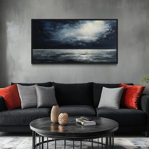 a modern living room with a black sofa adorned with red and gray throw pillows, a round black coffee table, and a large black-framed painting of a night sky hanging on the wall above the sofa.