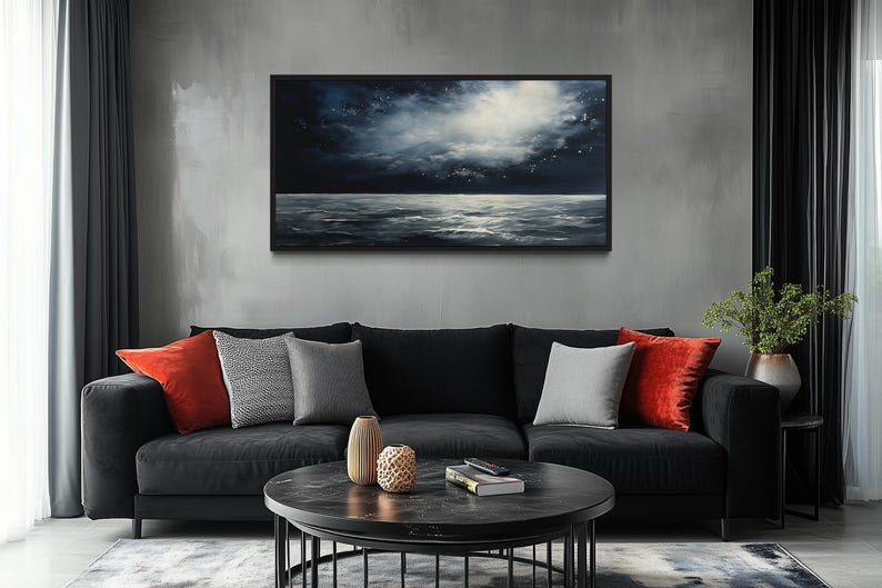 a modern living room with a black sofa adorned with red and gray throw pillows, a round black coffee table, and a large black-framed painting of a night sky hanging on the wall above the sofa.