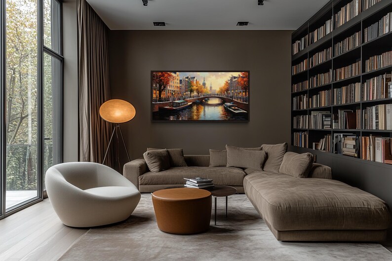 a modern living room with a large window overlooking a scenic view of a canal and trees. The room features a comfortable sofa, a round coffee table, and a floor lamp, creating a cozy and inviting atmosphere. A large bookshelf filled with books adds a touch of intellectual charm to the space. The room is illuminated by natural light from the window, enhancing the overall ambiance.