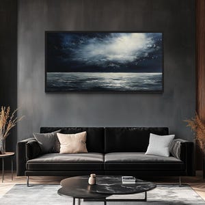 a modern living room with a large black sofa, a round coffee table, and a framed painting of a seascape hanging on the wall above the sofa.