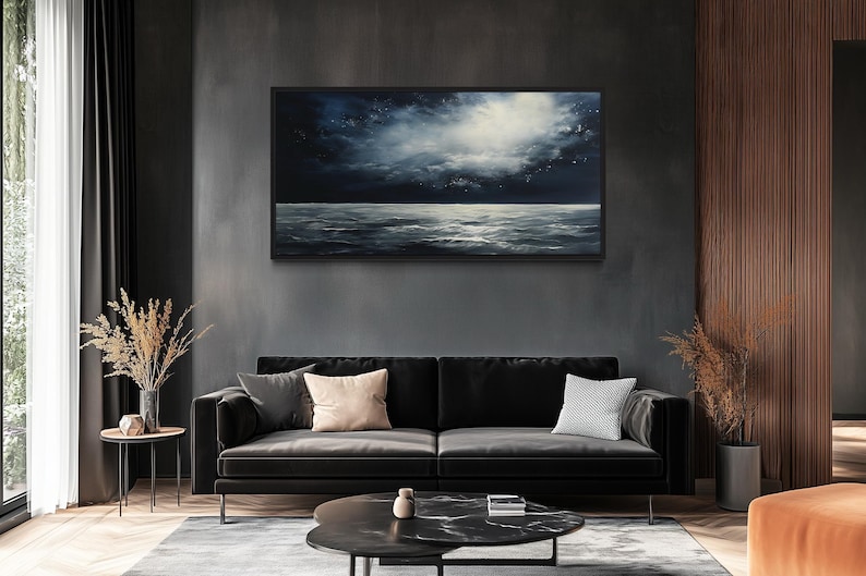 a modern living room with a large black sofa, a round coffee table, and a framed painting of a seascape hanging on the wall above the sofa.